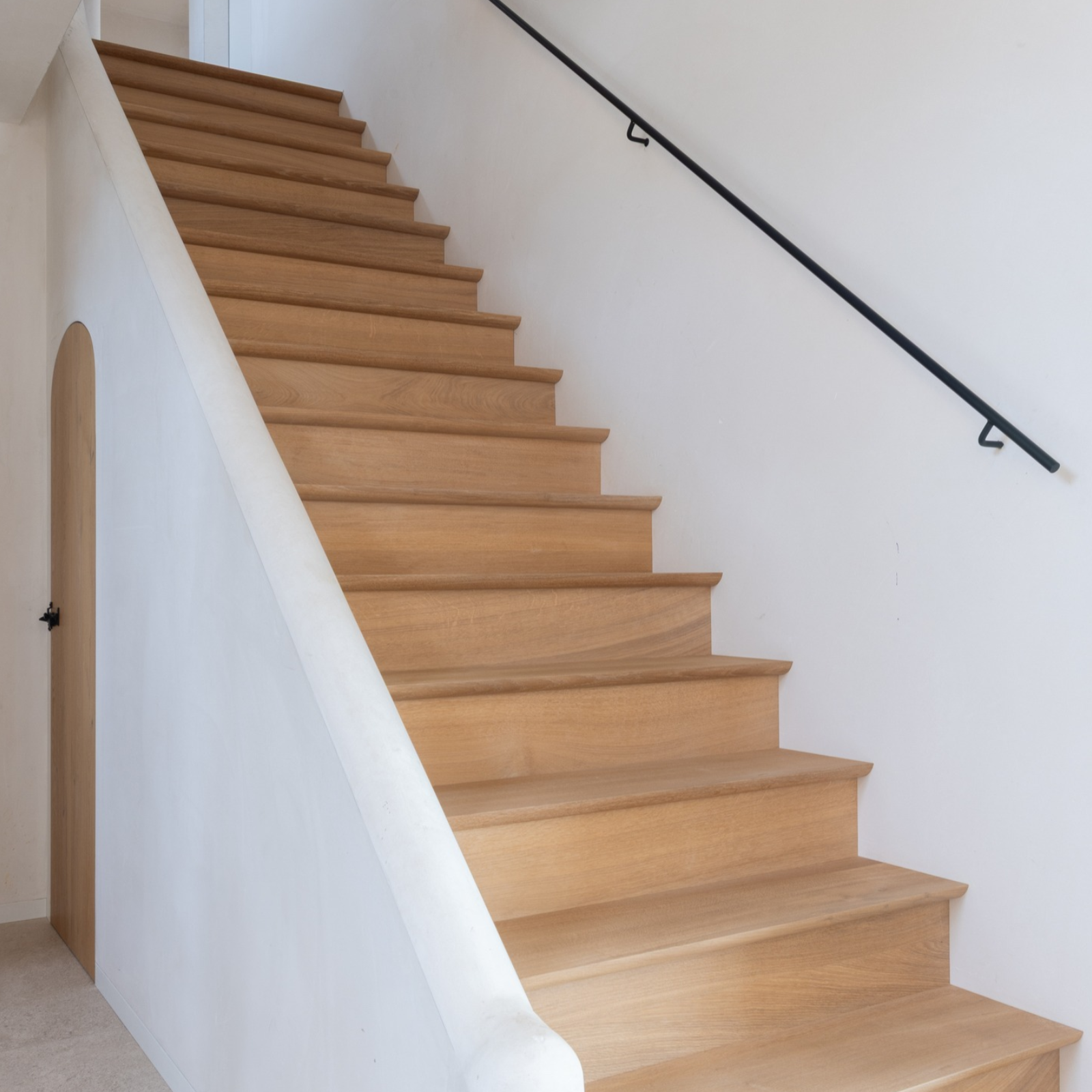 Traphal met eikenhouten trap, smeedijzeren trapleuning en afgeronde muur in mortex