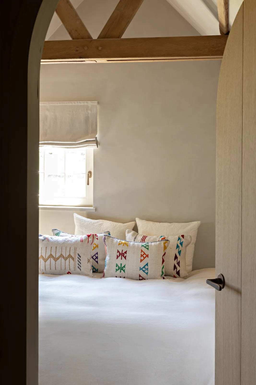 Slaapkamer met structuurverf op de muren, houten gebinte, linnen gordijnen en luxueus textiel